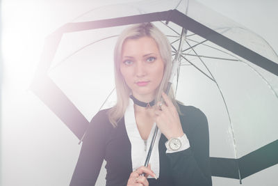 Portrait of young woman holding umbrella while standing against white background