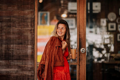 Portrait of young woman standing against glass door 