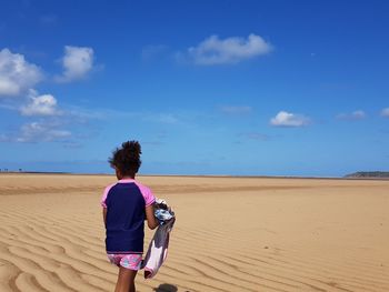 Rear view of girl standing at beach against sky