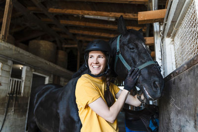 Smiling trainer with black horse in stable