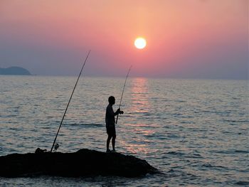 Silhouette of people fishing in sea during sunset