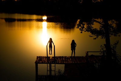 Silhouette people standing by lake against sky during sunset