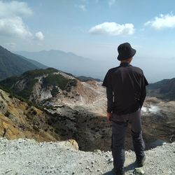 Rear view of man standing on mountain against sky