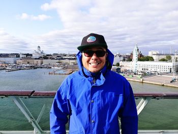 Portrait of smiling man standing against cityscape and cloudy sky