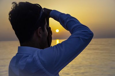 Rear view of man photographing sea during sunset