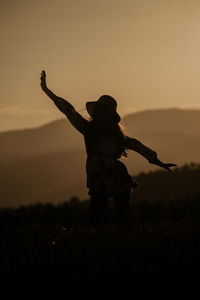 Rear view of silhouette man standing on field against sky during sunset