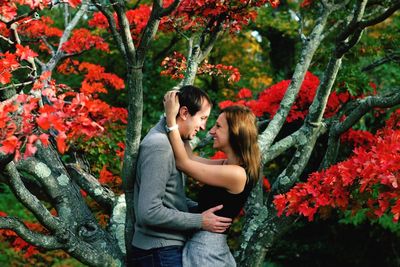 Young woman with man and red flowers against trees