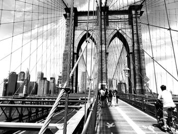 People on suspension bridge against sky in city