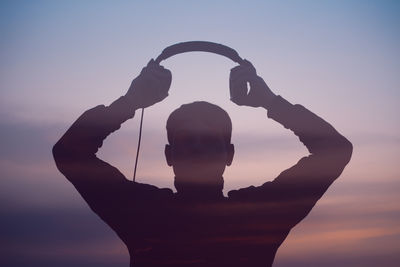 Low angle view of silhouette man with arms raised against sky during sunset