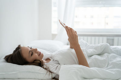 Woman using phone while lying on bed