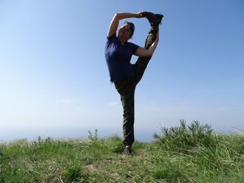 Woman doing yoga on field against blue sky