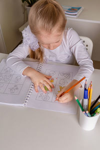 A girl student sits at a desk in the classroom and paints a picture with pencils. back to school 