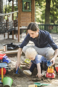 Father and son playing with toys on sand in playground at park during sunny day