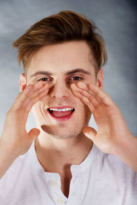 Young man whispering against gray backdrop