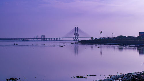 Cranes on bridge over sea against sky during sunset