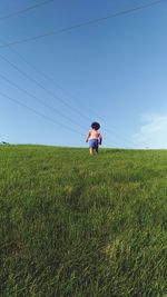 Rear view of girl standing on field against clear sky
