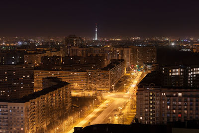 Night photo of street with lighted lanterns and tall residential buildings. illuminated tv tower