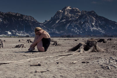 Woman sitting on desert against mountains