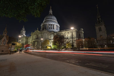 Light trails on street against illuminated buildings at night