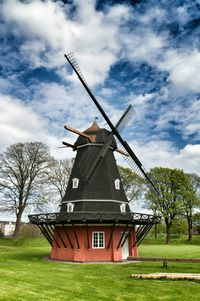 Low angle view of windmill on field against cloudy sky