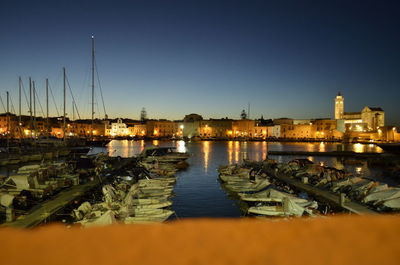 Sailboats moored on river by illuminated buildings against clear sky at night