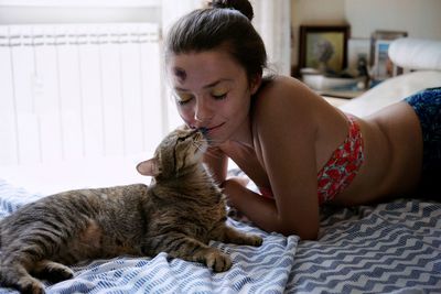 Woman lying with cat on bed at home