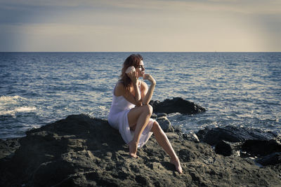 Woman in white dress sitting on some rocks by the sea