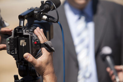 Cropped image of cameraman holding camera while interviewing politician