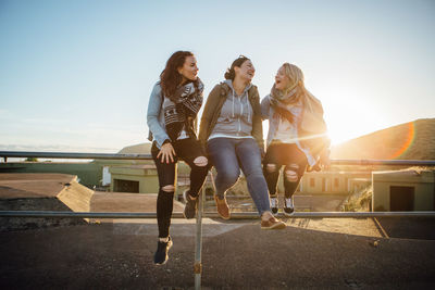 Women sitting on wall against clear sky