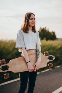 Young woman holding skateboard on road