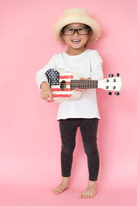 Girl playing guitar against pink background