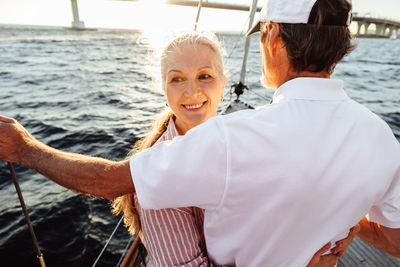 Smiling senior couple embracing in sailboat against sky