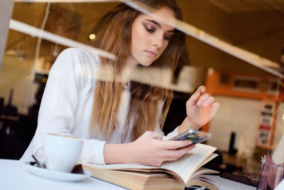 Teenage girl using mobile phone seen through window