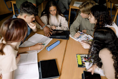 Teenage boys and girls studying together over digital tablet on school