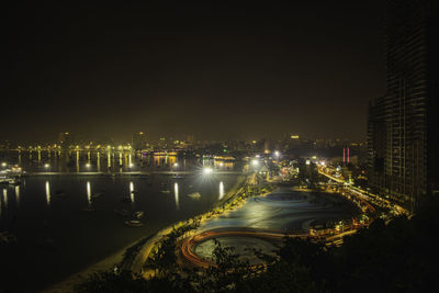 Illuminated city by river against sky at night