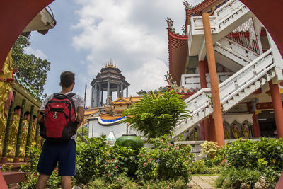 Rear view of man standing by building against sky