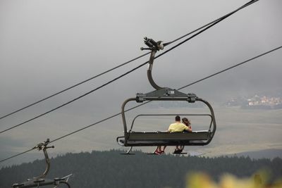 People sitting on ski lift against cloudy sky