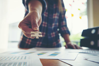 Midsection of woman holding jigsaw piece on table