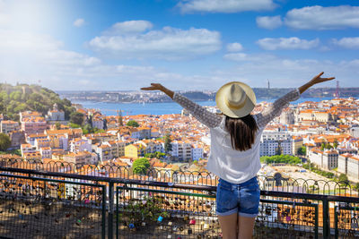 Rear view of woman with arms outstretched standing against cityscape