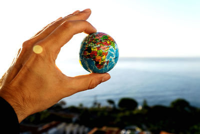 Close-up of hand holding crystal ball against sea