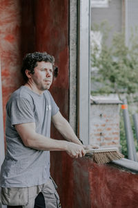 Caucasian male builder sweeps a window frame with a broom.