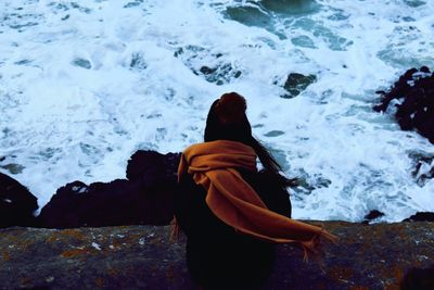 Rear view of woman sitting by sea on rock