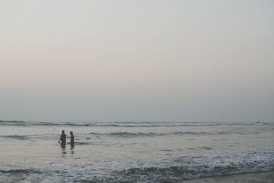 People standing on beach against clear sky