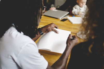 Rear view of businessman writing in book while discussing with female colleague in creative office