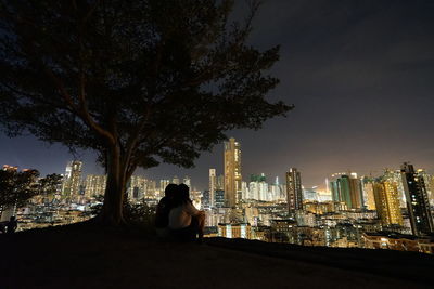 Rear view of man sitting against modern buildings in city