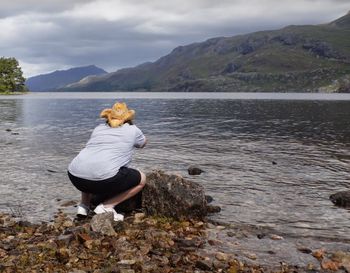 Rear view of woman on rock by lake against sky