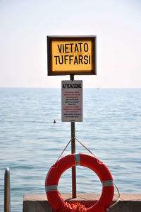 Information sign by sea against sky