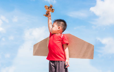 Boy holding toy while standing against sky