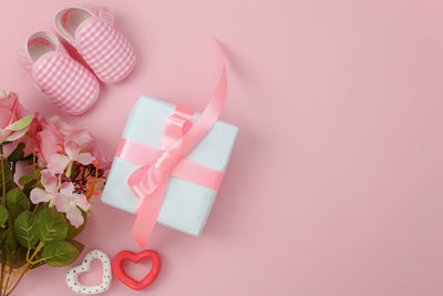 Directly above shot of gift box and shoes with flowers on pink background