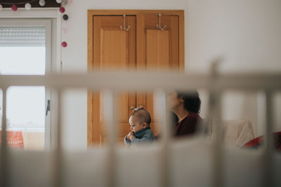 Mother with baby boy sitting at home seen through crib